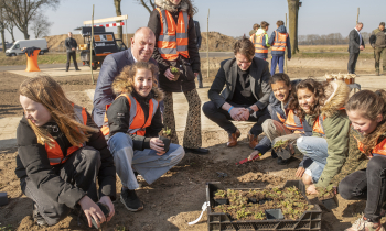 Gedeputeerde Bert Boerman helpt met de kinderen mee om de plantjes aan te planten rondom het bijenhotel op de duurzame carpoolplek.jpg